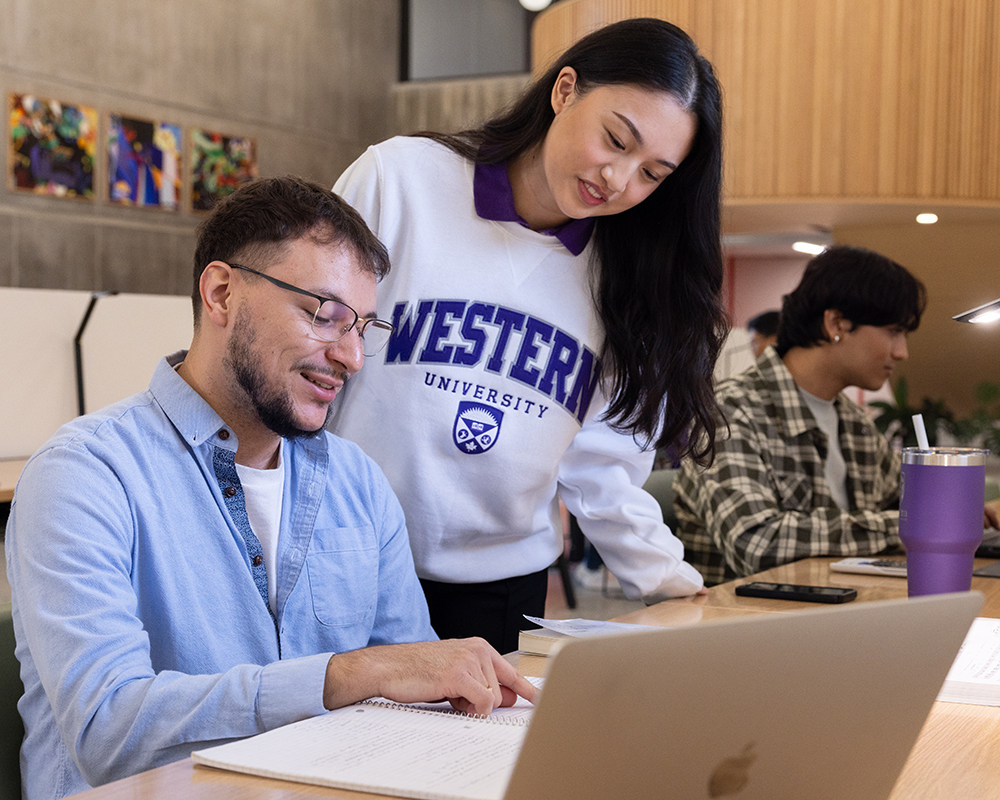 Students talking in the library over a laptop.
