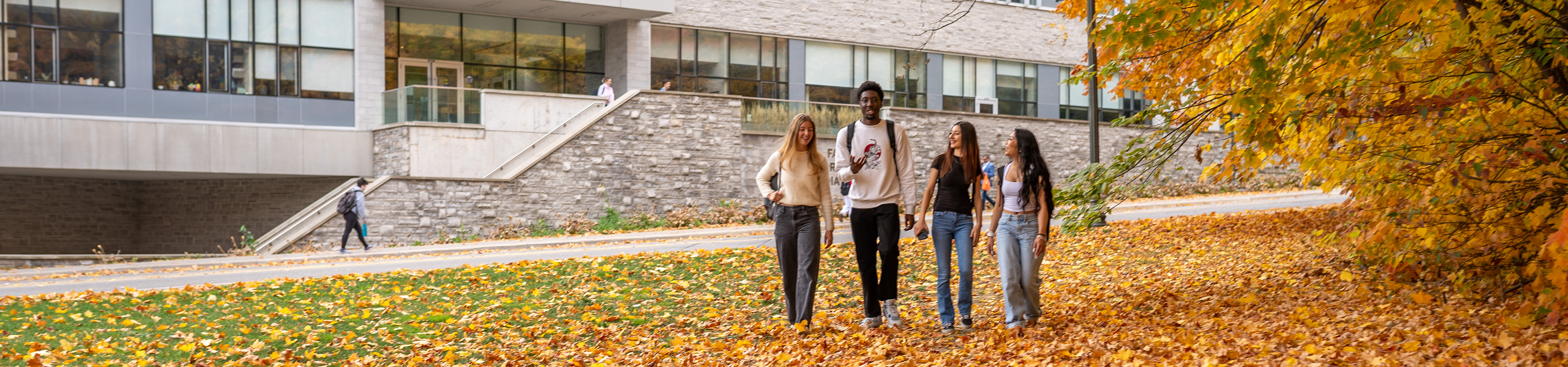 Students walking outside the FIMS & Nursing Building in the fall with orange leaves all around.