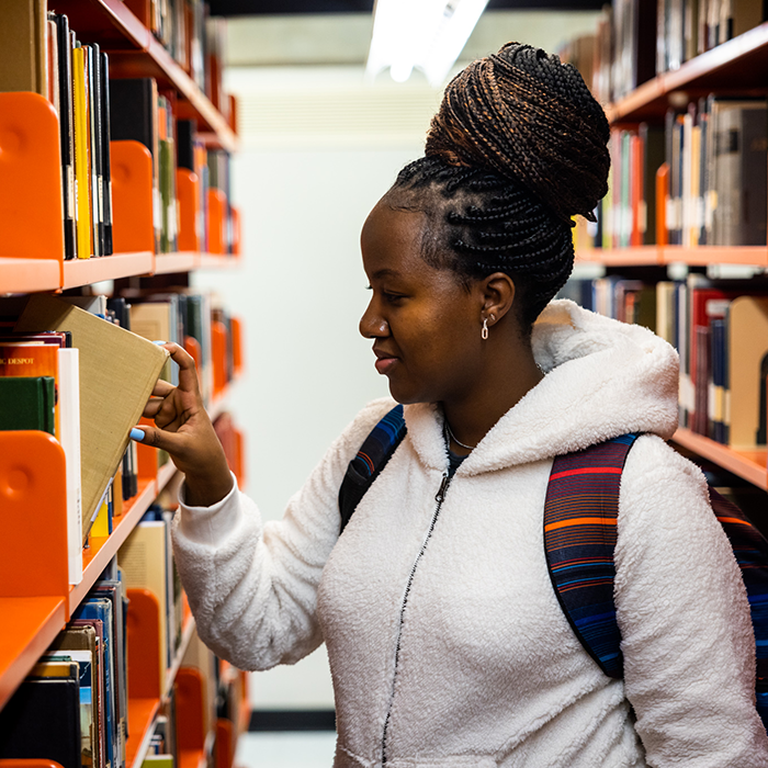 A student pulling a book off a shelf in the library stacks