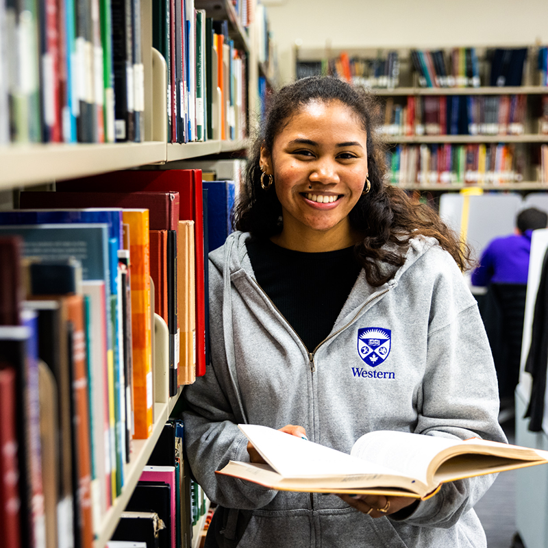 A young female student posing beside a row of books